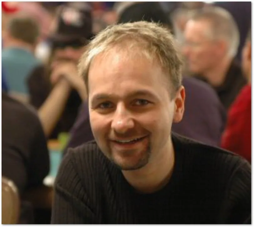 Daniel Negreanu ler mot kameran vid ett pokerbord med otydlig bakgrund